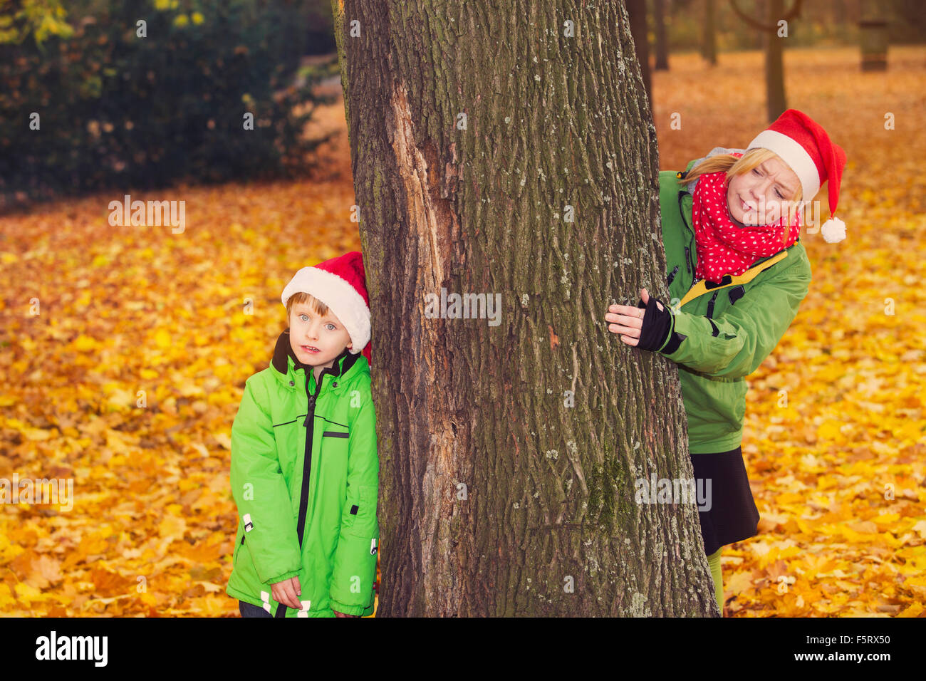 Mutter und Sohn mit Santa Hüte suchen um einen Baum im Park im Herbst Stockfoto