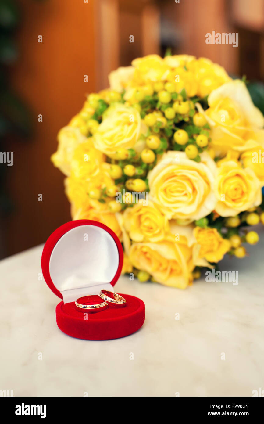 Trauringe im roten Fall auf einem Hintergrund von gelben Brautstrauß Stockfoto