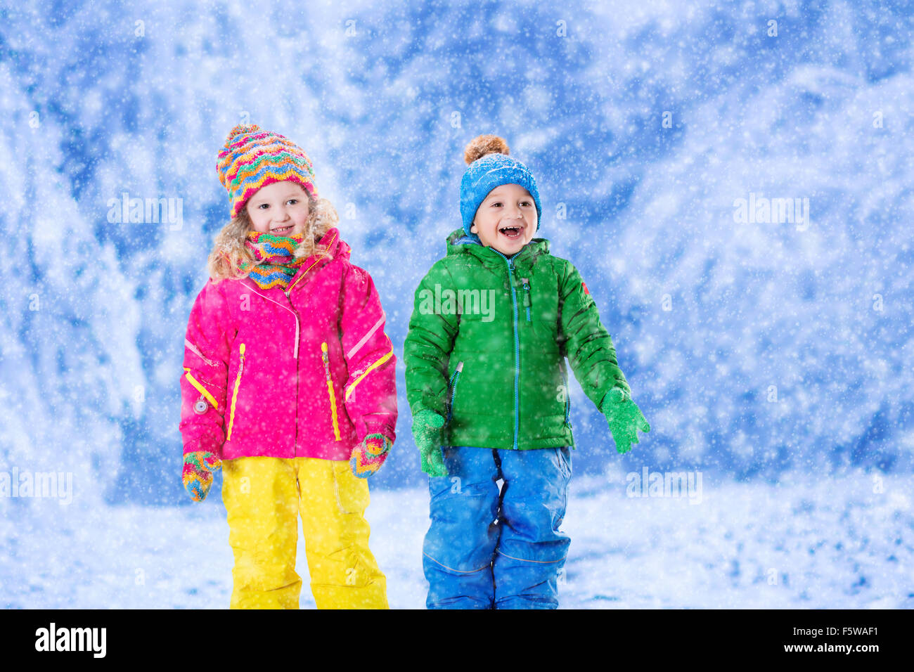 Kleine Mädchen und jungen in bunten Hut fangen Schneeflocken im Winter Park am Heiligabend. Skiurlaub für Familien mit Kindern. Stockfoto