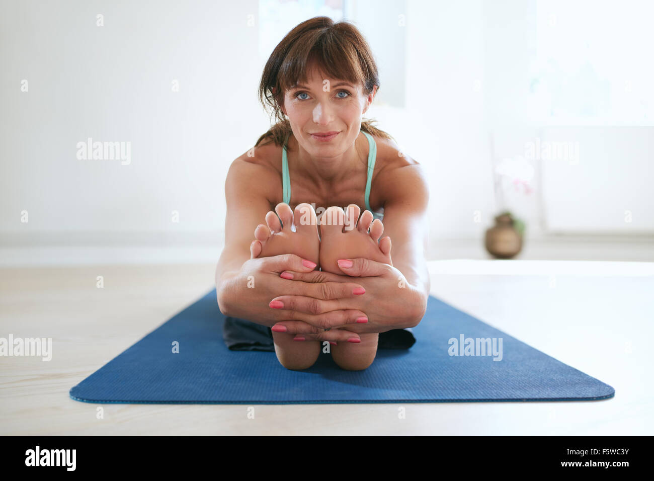 Frau im sitzen nach vorne beugen Yoga Pose halten Füße. Fitness-Trainer üben Paschimottanasana Yoga Training im Fitness-Studio. Stockfoto