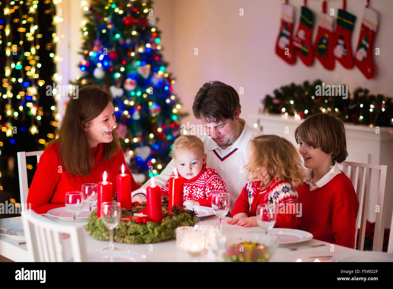Große Familie mit drei Kindern zu Hause Weihnachten zu feiern. Festliches Abendessen am Kamin und Weihnachtsbaum. Eltern und Kinder essen Stockfoto