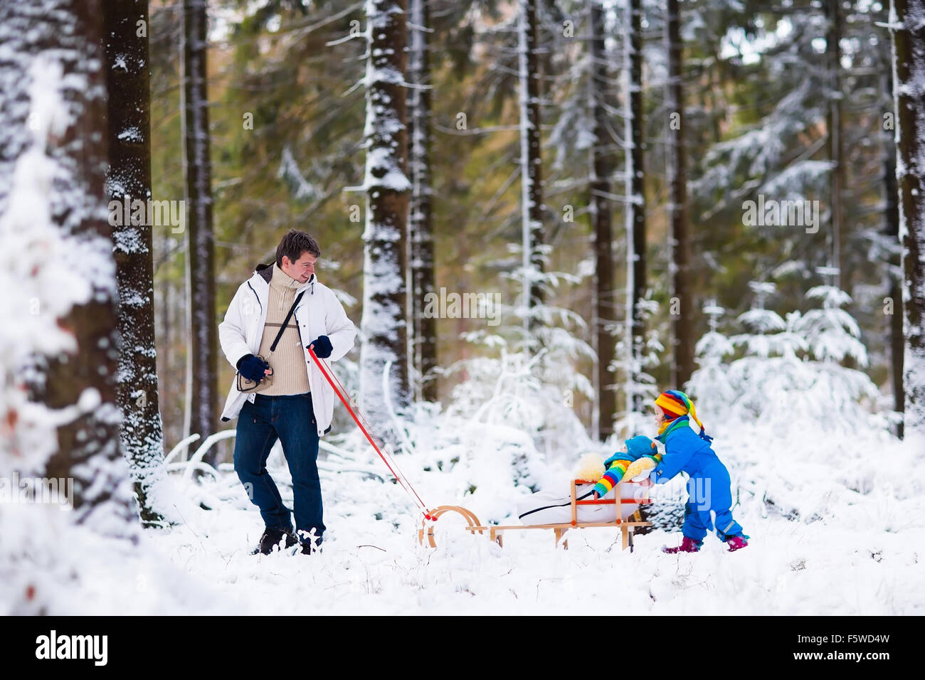Vater und Kinder genießen Schlittenfahrt im Winterwald. Baby Boy und Kleinkind Mädchen Schlitten im verschneiten Park. Papa ziehen Kinder auf Schlitten Stockfoto