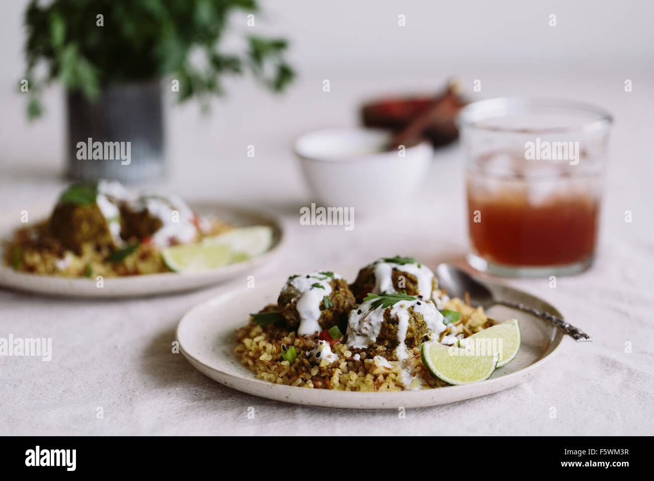 Curry Linsen-Frikadellen serviert auf Bulgur-Pilaw und gekrönt mit Joghurt-Sauce werden auf einem gedeckten Tisch angezeigt. Stockfoto
