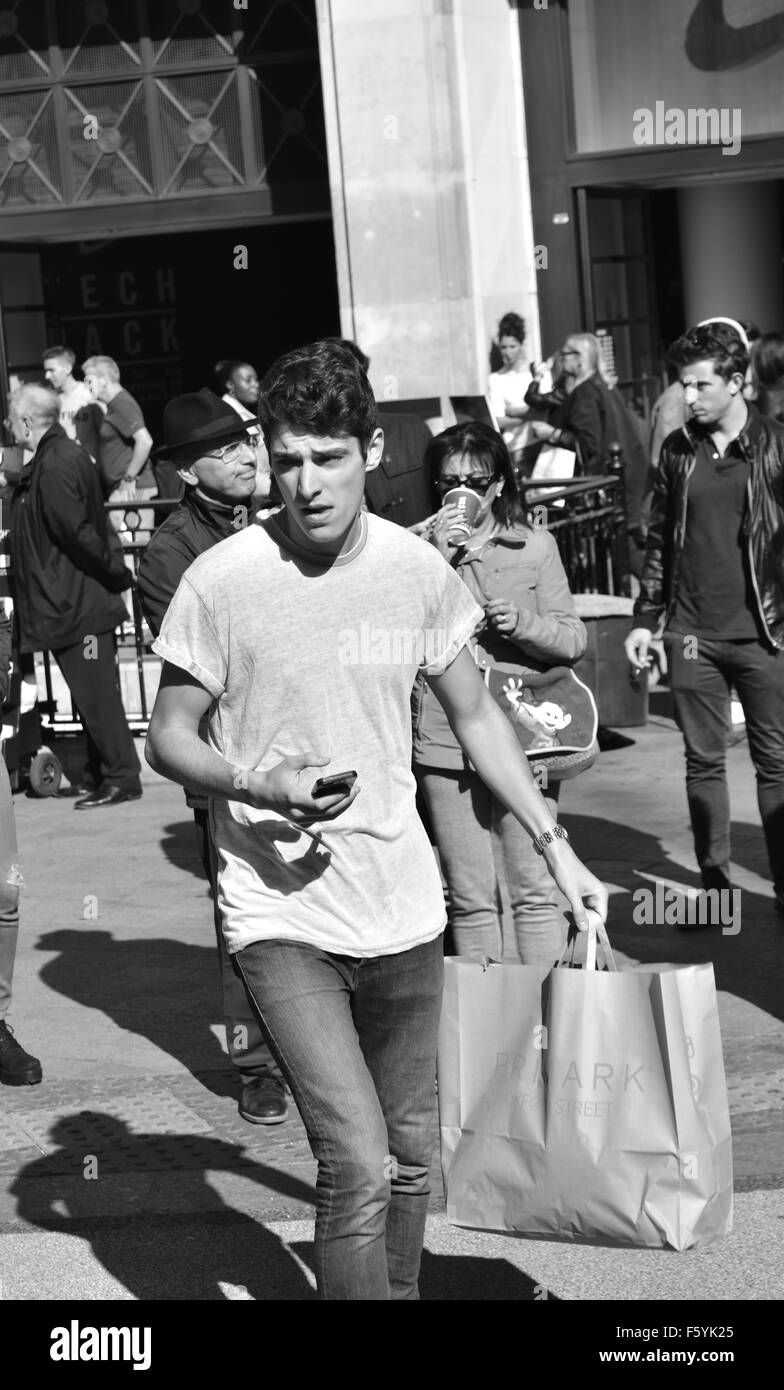 B&W, man Carrying Shopping Bag und Mobile, Running Across, Oxford Street, London, England, GB, GB. Stockfoto