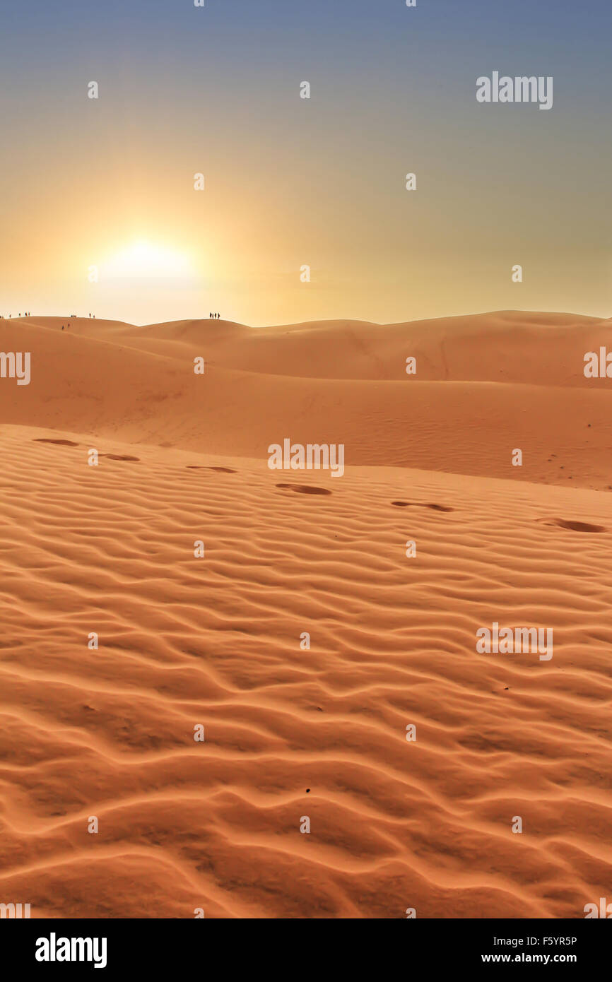 Wüstenlandschaft, Sonnenuntergang hinter Dünen, Menschen Silhouetten im Hintergrund und Fußspuren im sand Stockfoto