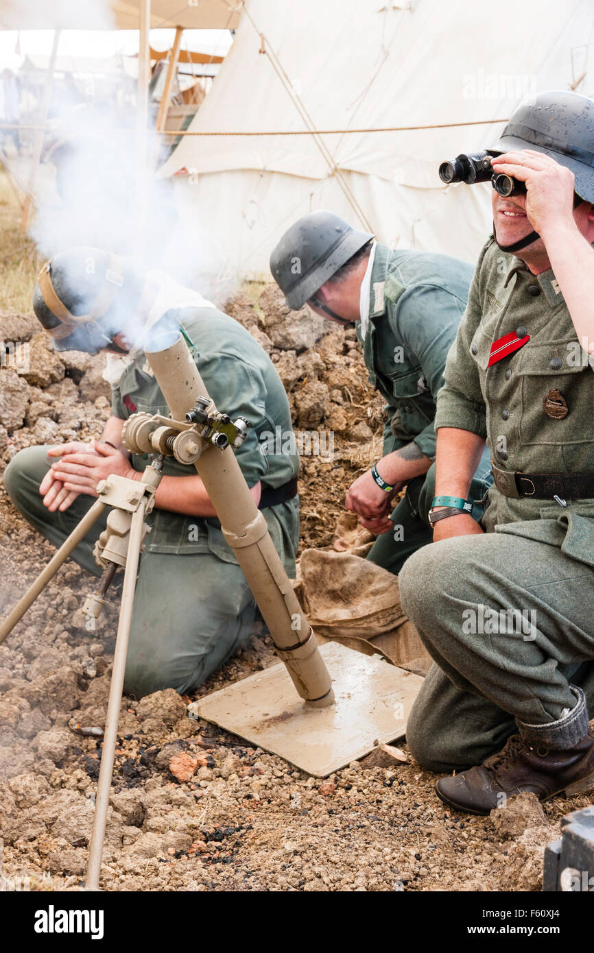 Weltkrieg zwei Re-enactment. Deutsche Soldaten feuern 8 cm Licht graben Mörtel in Grub während Offizier durch ein Fernglas sieht den Schuß zu verfolgen. Stockfoto