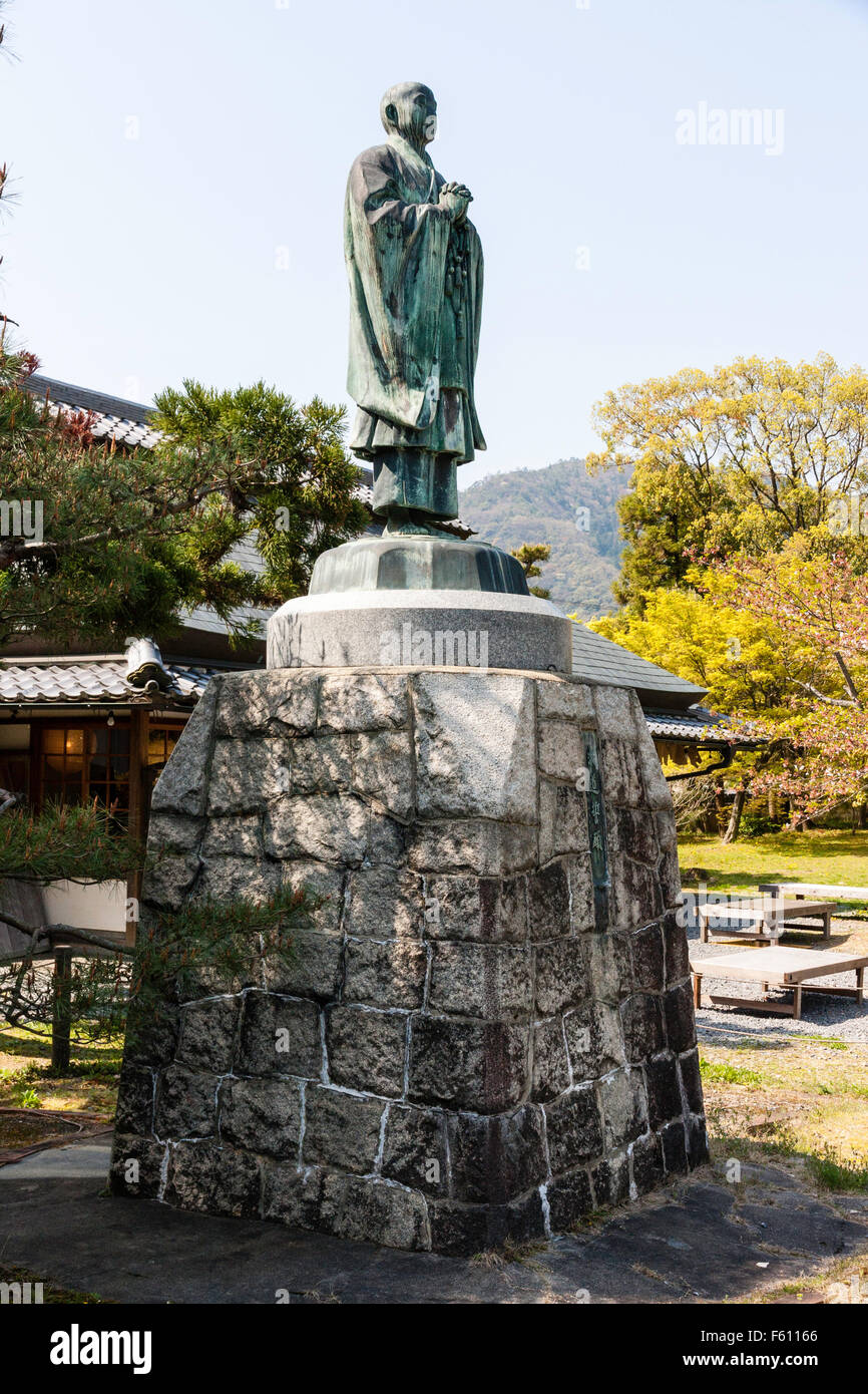 Japan, Kyoto, Seiryo-ji Temple. Saga Shakado. Bronzestatue von Priester, auf Sockel aus Stein auf Stein im Garten. Strahlend blauer Himmel. Stockfoto