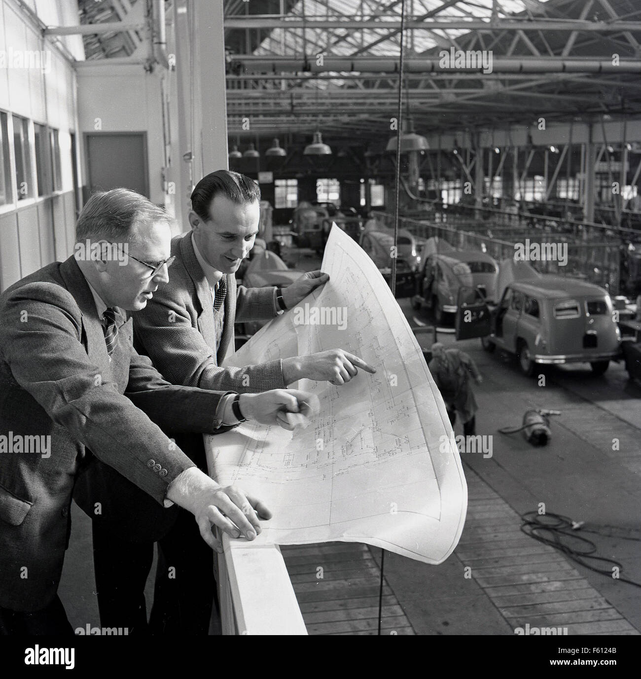 Geschichtsbild der 1950er Jahre, zwei Führungskräfte oder Manager der British Motor Corporation oder BMC studieren Fertigungsplänen oder Diagramme, mit Blick auf den van-Produktionsstraße. Stockfoto