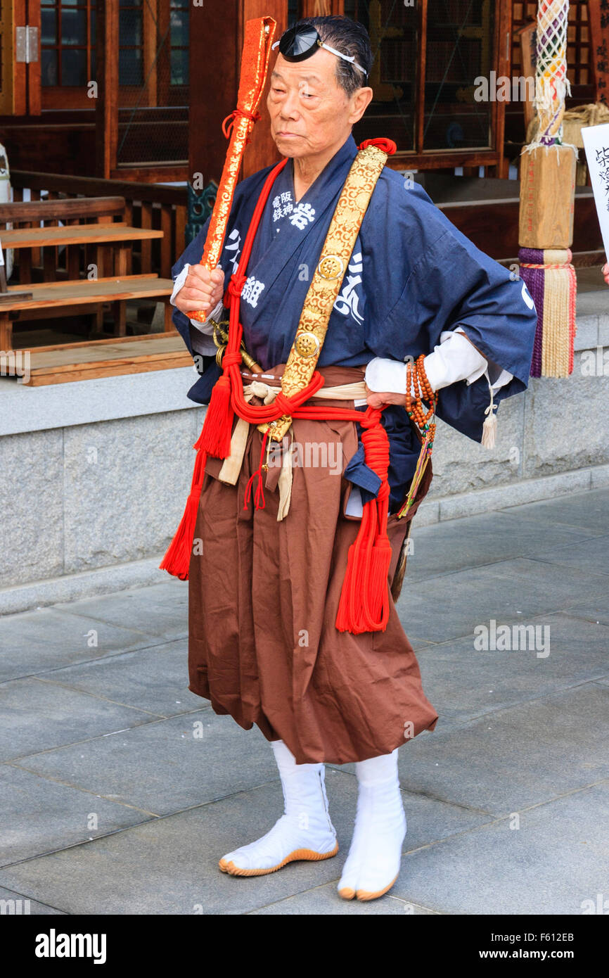 Japan, Nishinomiya, Tokoji Shotaizan Tempel. Priester im Krieger Mönch Kostüm, Yamabushi, blaue Tunika, braune Hose, stehend außerhalb Temple Hall. Stockfoto