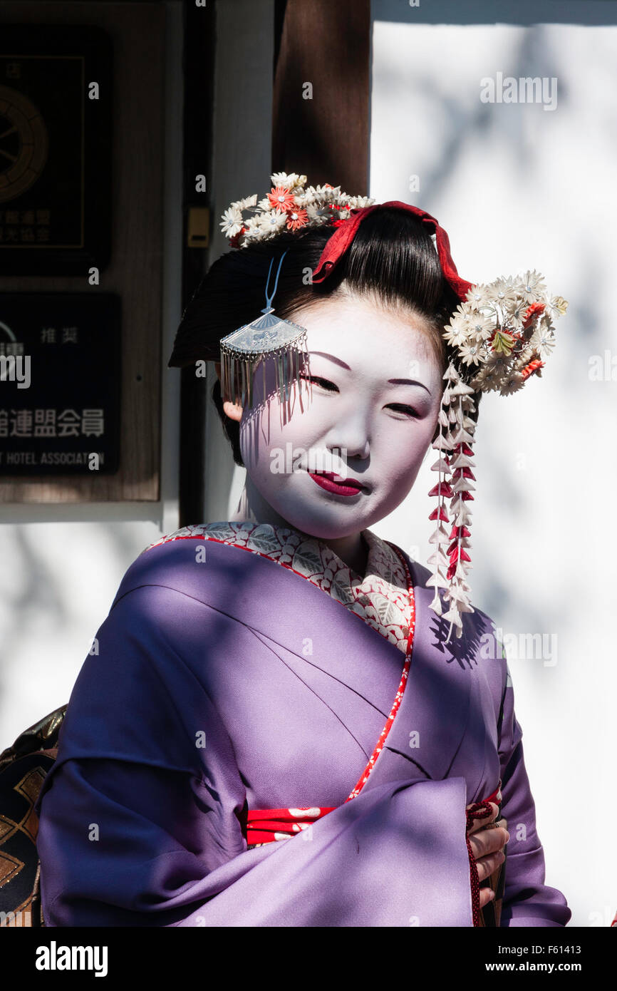 Japan, Kyoto. Japanische reifen Geisha, Maiko, ihr Gesicht im Viewer im hellen Sonnenlicht zu schauen, sich zu drehen. Lila Kimono. Kopf und Schultern. Stockfoto
