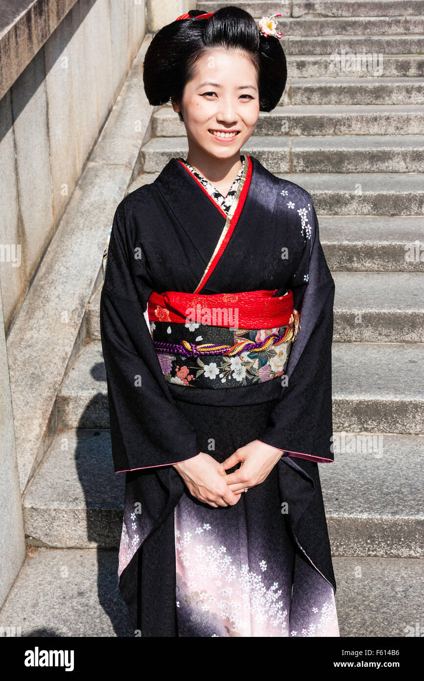 Japan, Kyoto. Reife Frau, in Schwarz mit roten Kimono obi Schärpe, im  Sonnenlicht auf Steinstufen, lächeln und posieren. Zeigt. Keinen  Blickkontakt Stockfotografie - Alamy