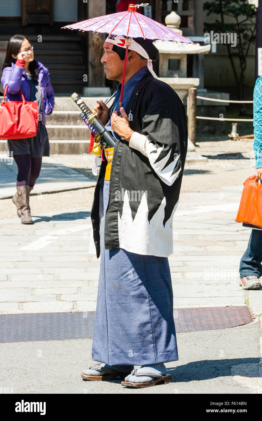 Japan, Kyoto. Kiyomizu dera Tempel. Seitenansicht der Mann, der  Sonnenschein, das Tragen eines Samurai Mantel mit Schwert und Holding rosa  Regenschirm als Sonnenschirm Stockfotografie - Alamy