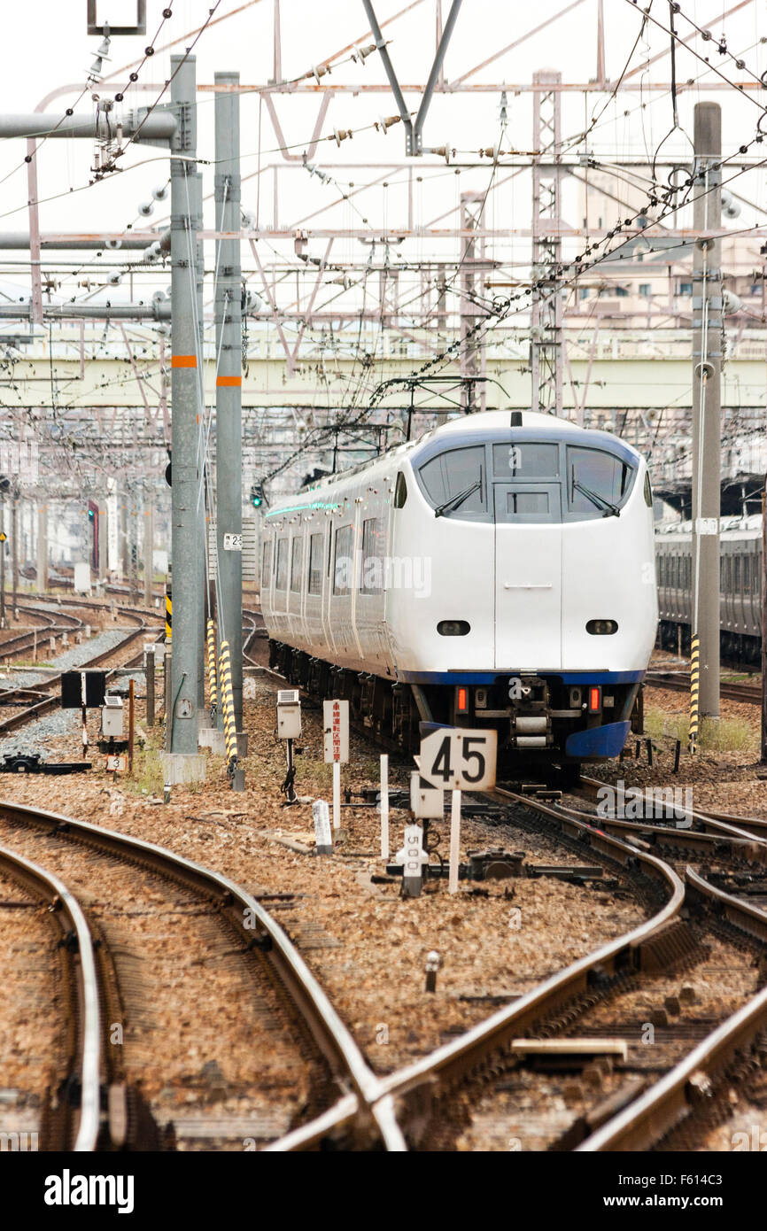 Japan, Osaka. Weiße JR Pendlerzug nähern. Tele-shot, entlang der Schienen und Kabel. Trübes Wetter. Stockfoto