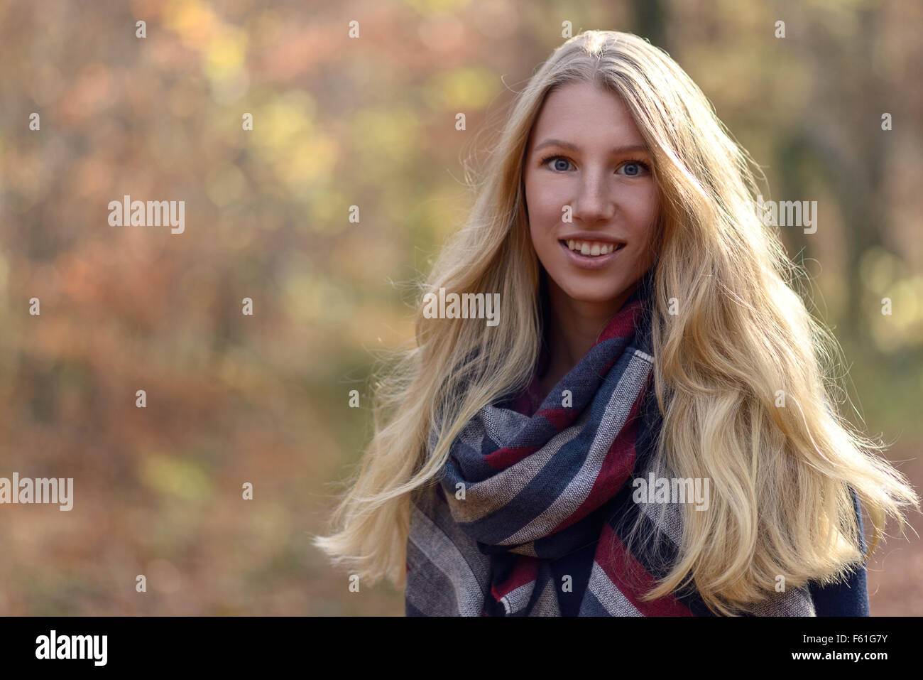 Attraktive junge Frau mit langen blonden Haaren im Herbst Mode tragen einen trendigen Schal stehen im Freien im Herbst Wald lächelnd Stockfoto