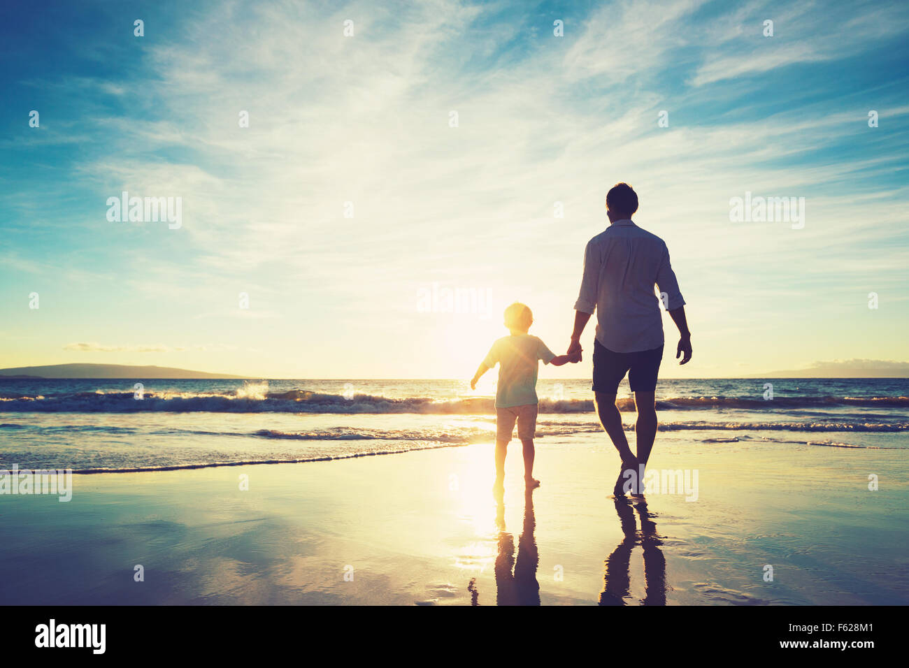 Vater und Sohn Hand in Hand zusammen spazieren am Strand bei Sonnenuntergang Stockfoto