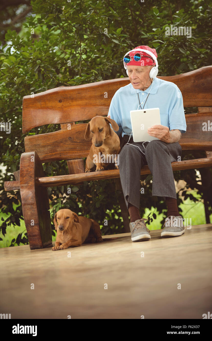 Älterer Mann mit Kopftuch, Sonnenbrillen und Kopfhörer, hören Rock'n'Roll auf dem Tablet. Stockfoto