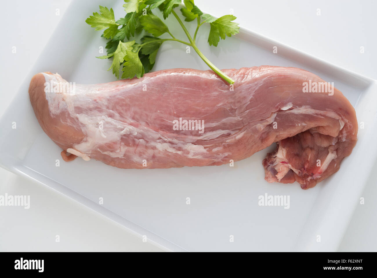 rohes Schweinefleisch Filet auf einem weißen Teller und mit Petersilie garniert Stockfoto
