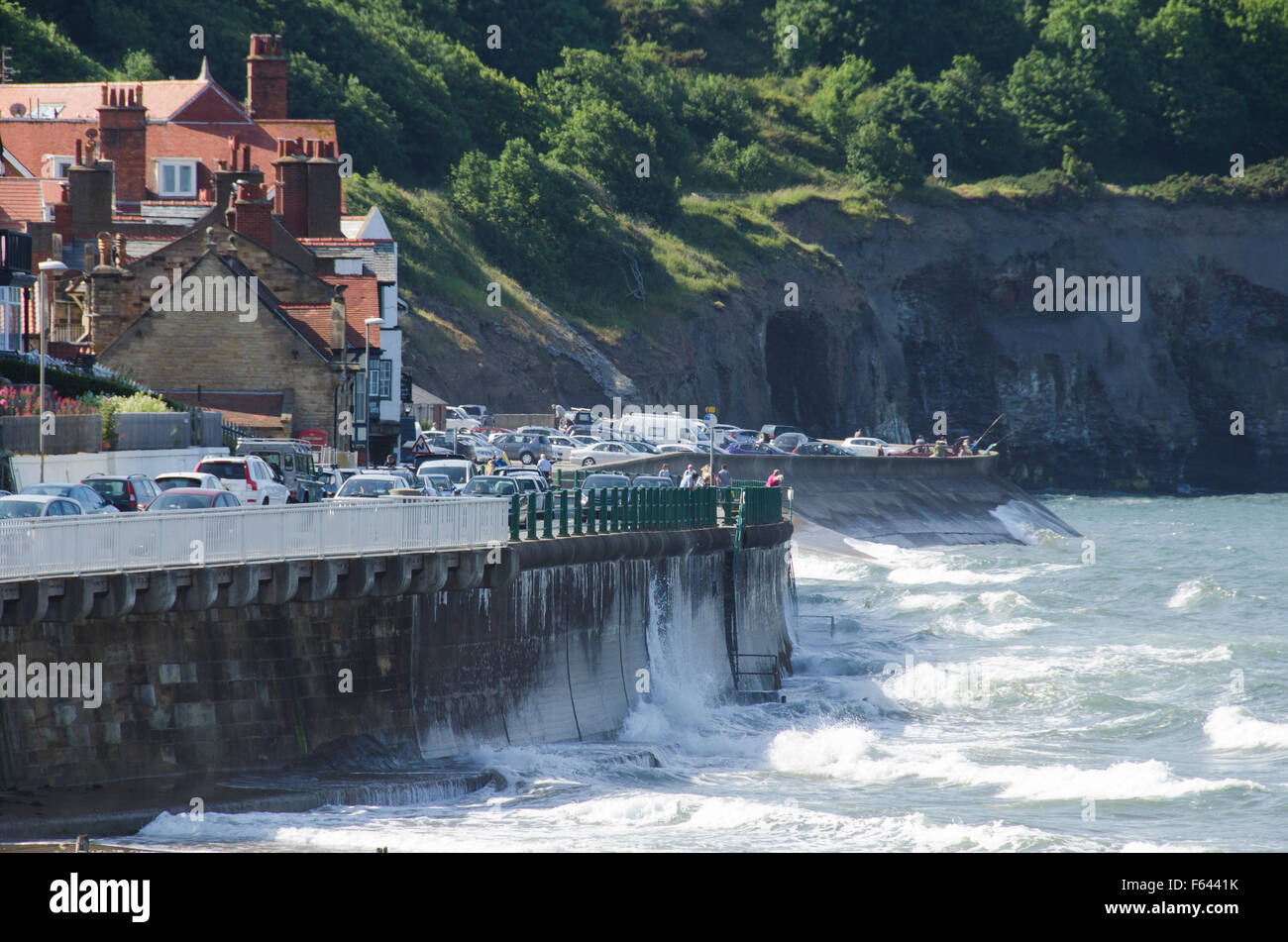 Sonnige Aussicht auf Whitbys, North Yorkshire coast, GB, UK - Wellen brechen gegen den Deich, die Küstenstraße mit Autos beschäftigt und die Klippen hinaus. Stockfoto