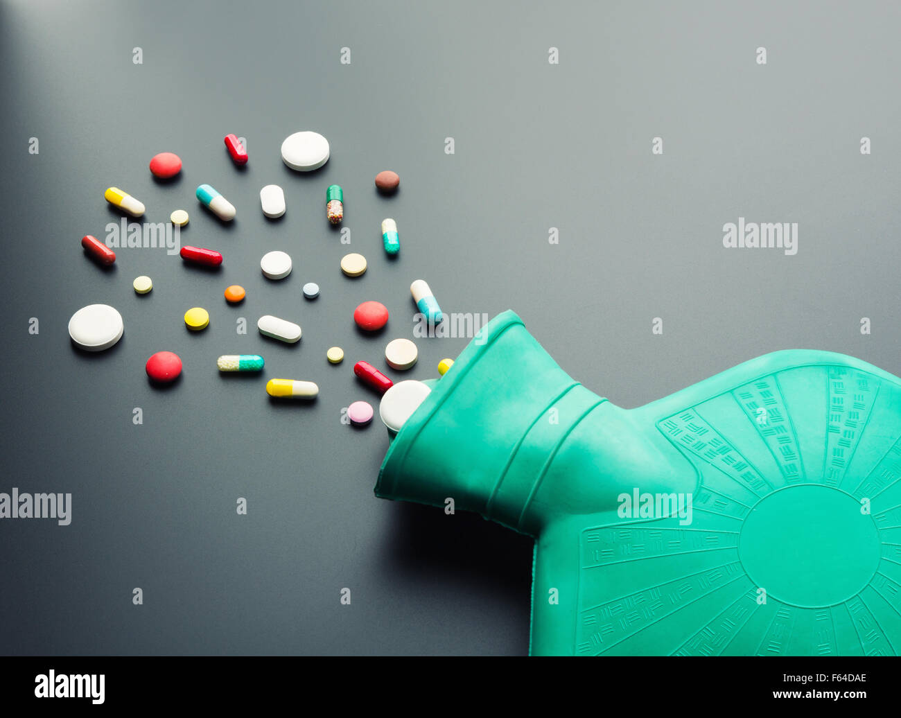 Grüne Gummi-Wärmflasche mit Pillen auf grauem Hintergrund Stockfoto