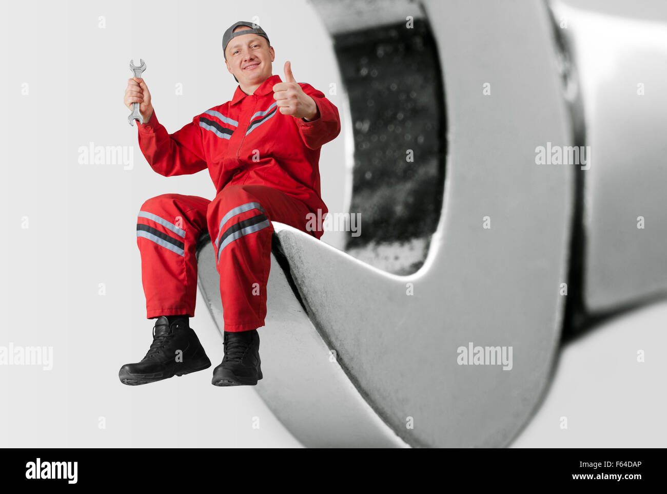 Glücklich Mechaniker sitzen in großen Schraubenschlüssel und Ordnung Geste zeigt Stockfoto