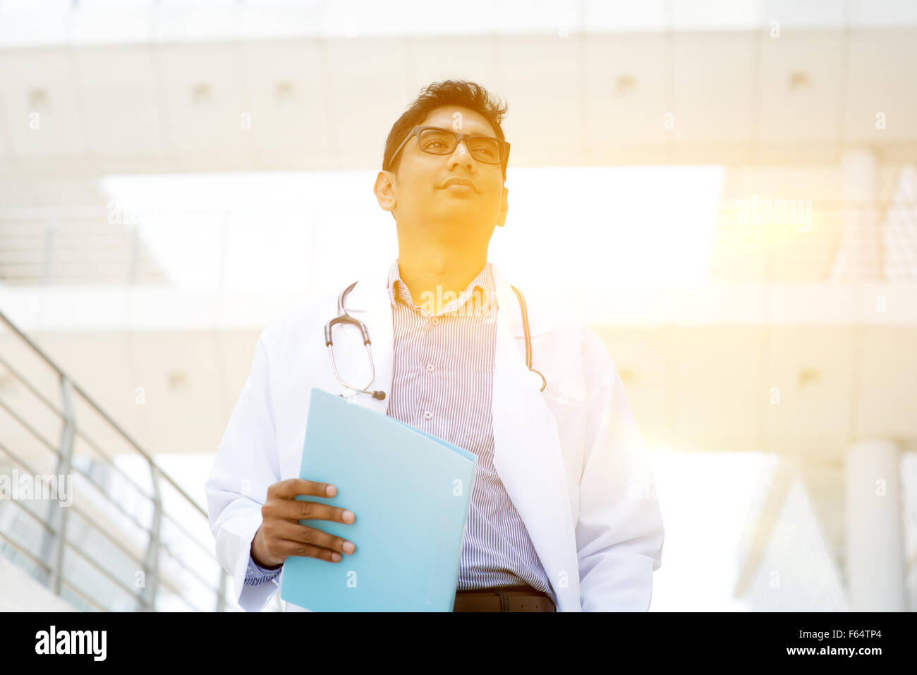 Asiatischen indischen Arzt außerhalb Klinikgebäude, schönen goldenen Sonnenlicht im Hintergrund stehen. Stockfoto