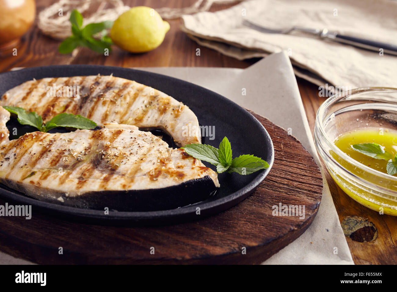 Gegrillter Schwertfisch Scheiben in einer gusseisernen Pfanne auf einem Holztisch, garniert mit Minze, Oregano, Salz und salmoriglio Stockfoto