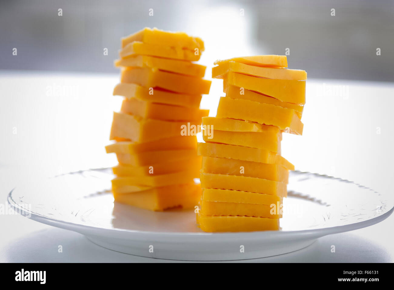 Stapel von chedder Käse auf einem weißen Teller angezeigt, weiß Tisch, mit einem Fenster im Hintergrund. Stockfoto