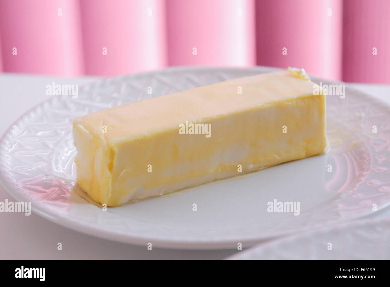 Butter oder Margarine auf einem weißen Keramikplatte mit rosa Jalousien im Hintergrund auf einem weißen Tisch. Stockfoto