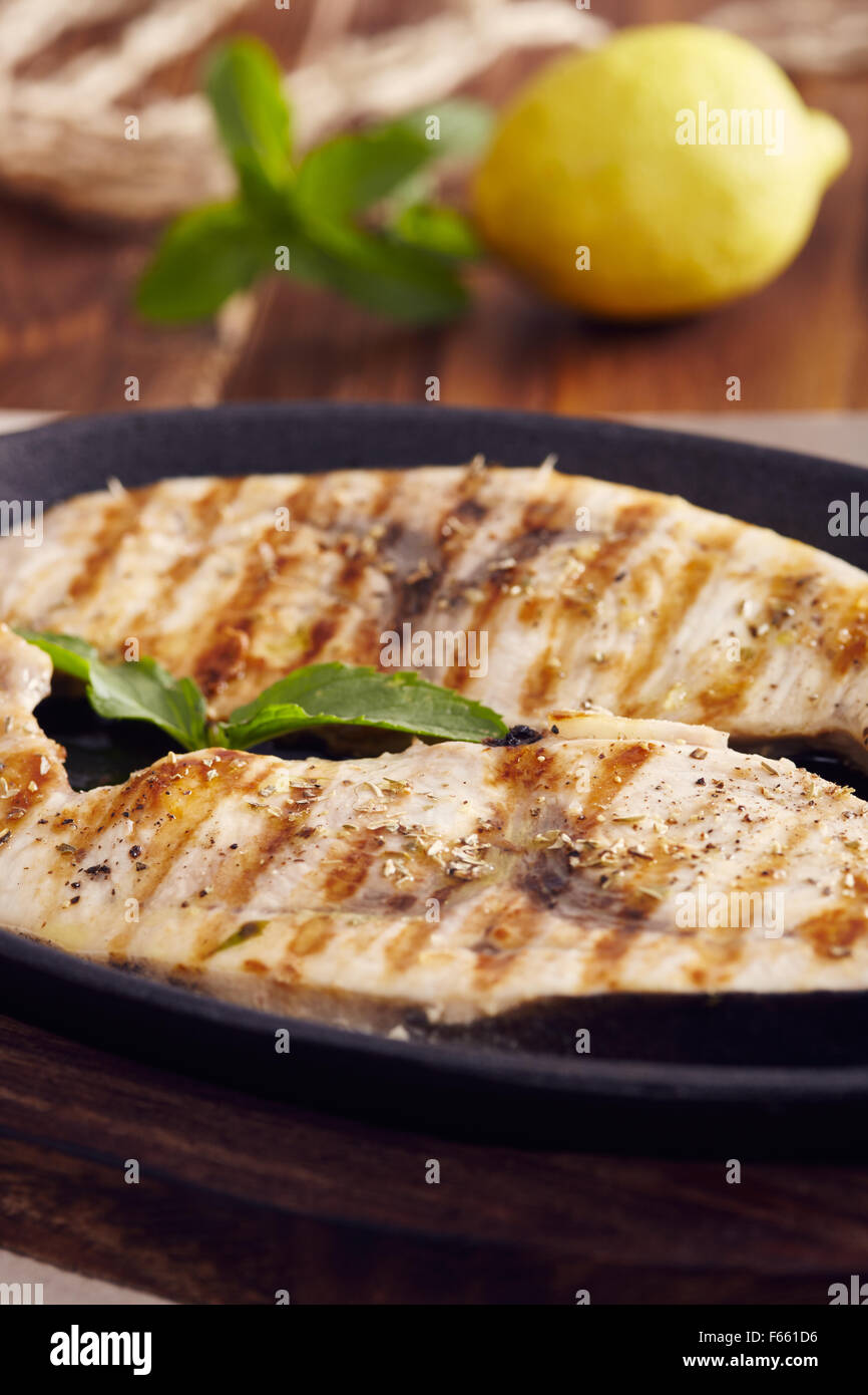 Gegrillter Schwertfisch Scheiben in einer gusseisernen Pfanne auf einem Holztisch, garniert mit Minze, Oregano, Salz und salmoriglio Stockfoto