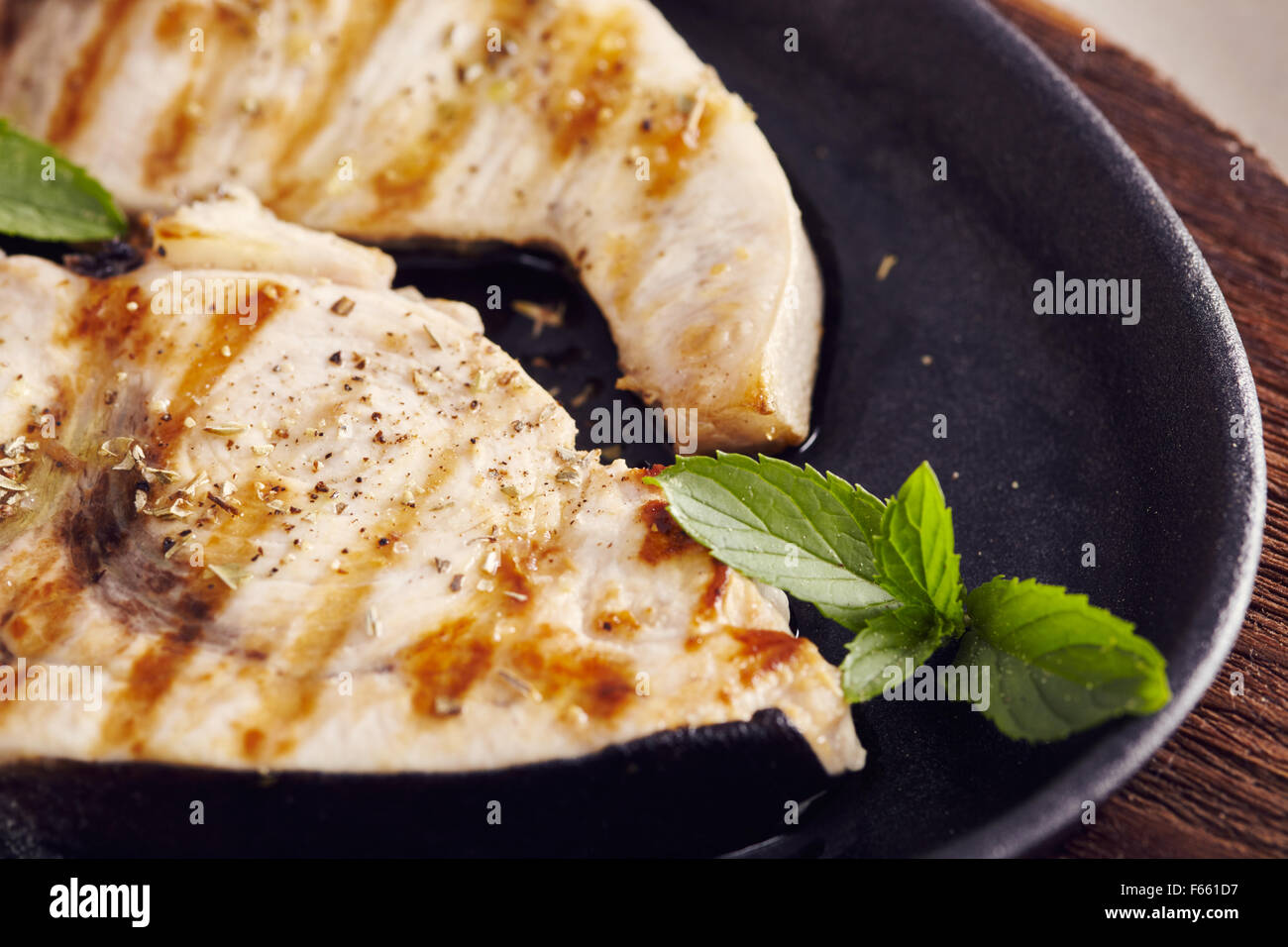 Gegrillter Schwertfisch Scheiben in einer gusseisernen Pfanne auf einem Holztisch, garniert mit Minze, Oregano, Salz und salmoriglio Stockfoto