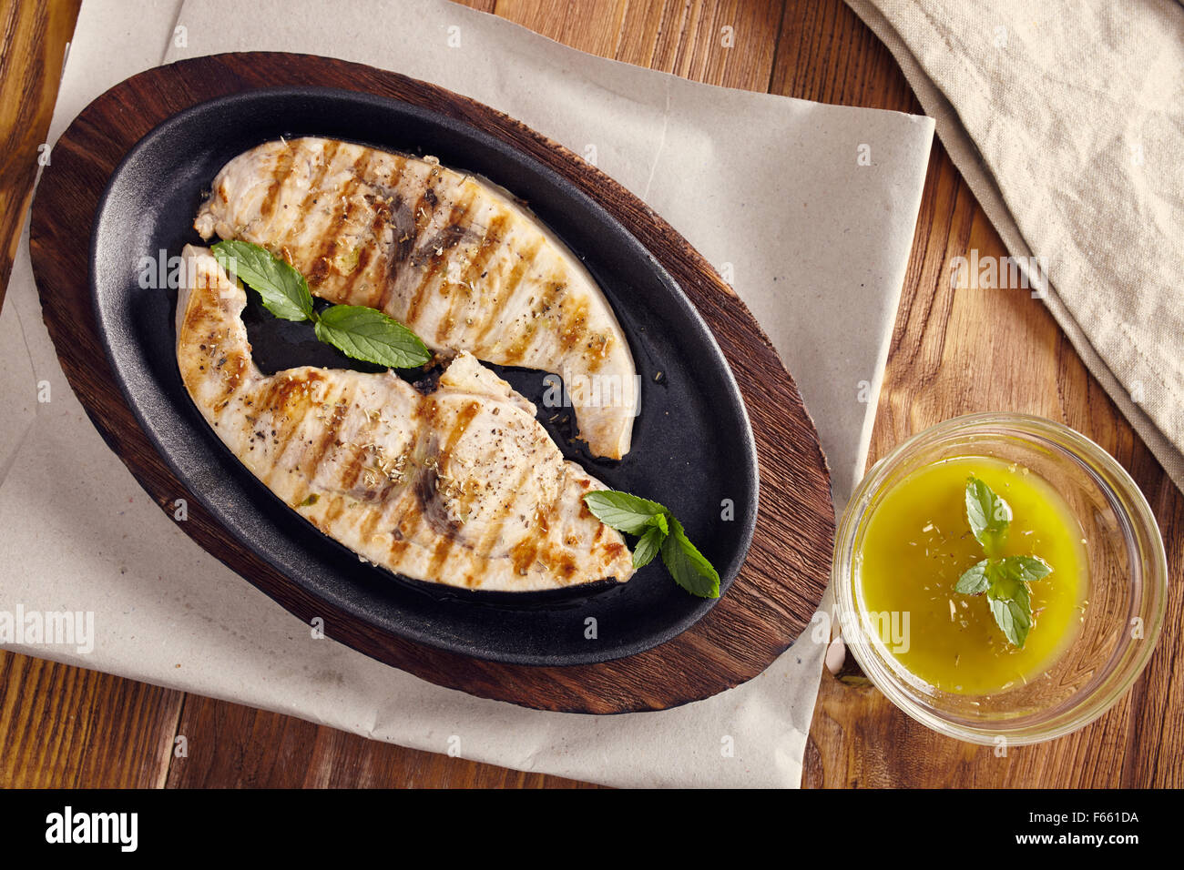 Gegrillter Schwertfisch Scheiben in einer gusseisernen Pfanne auf einem Holztisch, garniert mit Minze, Oregano, Salz und salmoriglio Stockfoto