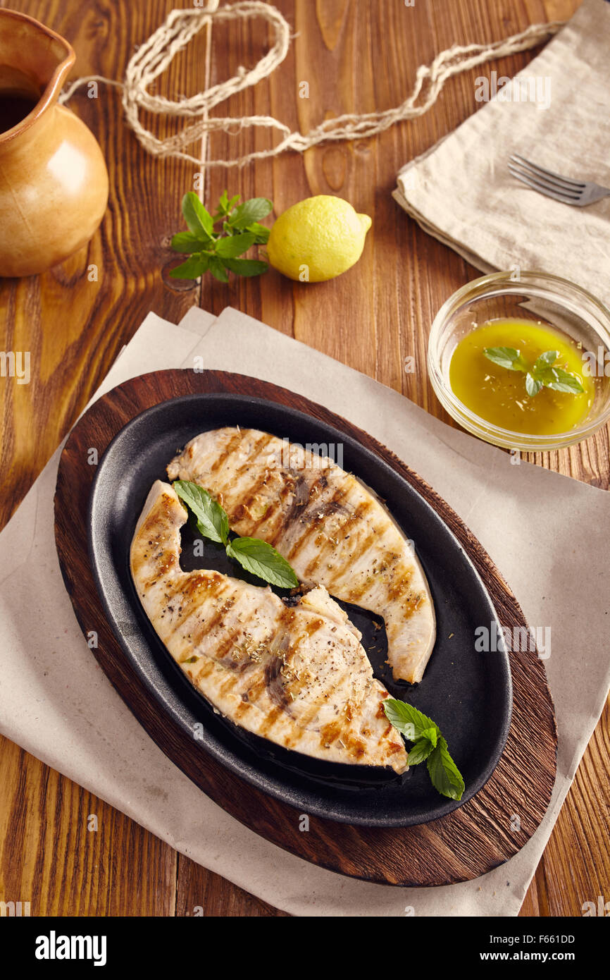 Gegrillter Schwertfisch Scheiben in einer gusseisernen Pfanne auf einem Holztisch, garniert mit Minze, Oregano, Salz und salmoriglio Stockfoto