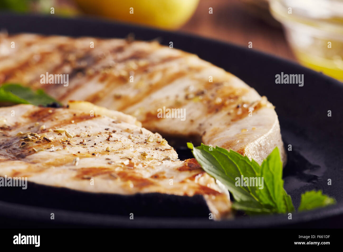 Gegrillter Schwertfisch Scheiben in einer gusseisernen Pfanne auf einem Holztisch, garniert mit Minze, Oregano, Salz und salmoriglio Stockfoto