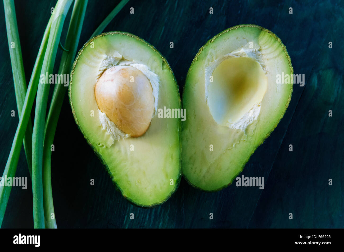 auf halbierte Avocado mit der Grube ausgesetzt auf einem blau-grünen Hintergrund mit Tabelle ergibt sich Zwiebel Rahmung Stockfoto