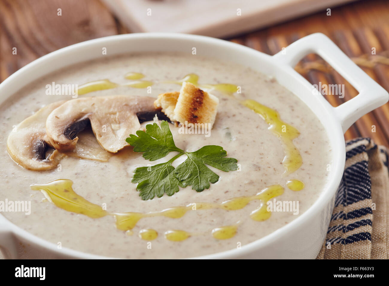 Champignon Cremesuppe auf einem Tisch mit Brot, Knoblauch und rohe Pilze auf einem Schneidebrett weiß. Salz und Pfeffer auf dem Tisch. Stockfoto