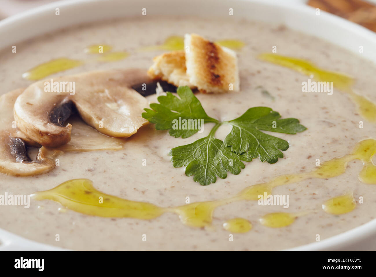 Champignon Cremesuppe auf einem Tisch mit Brot, Knoblauch und rohe Pilze auf einem Schneidebrett weiß. Salz und Pfeffer auf dem Tisch. Stockfoto