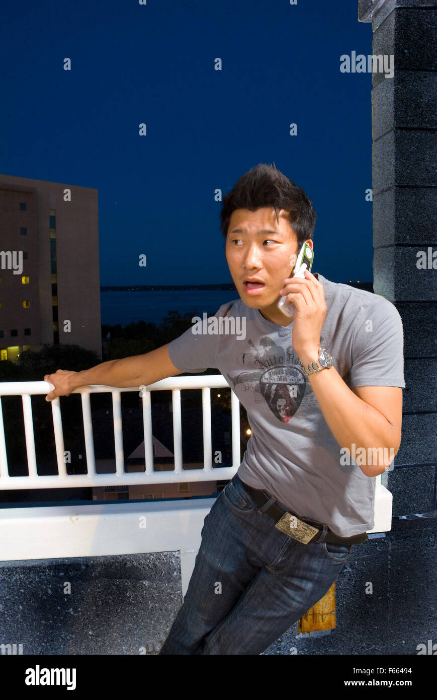 Asiatische Mann auf einem Flipchart Telefon oben auf einem Gebäude nachts. Er hat einen angeregten Ausdruck auf dem Gesicht. von der Kamera entfernt. Stockfoto