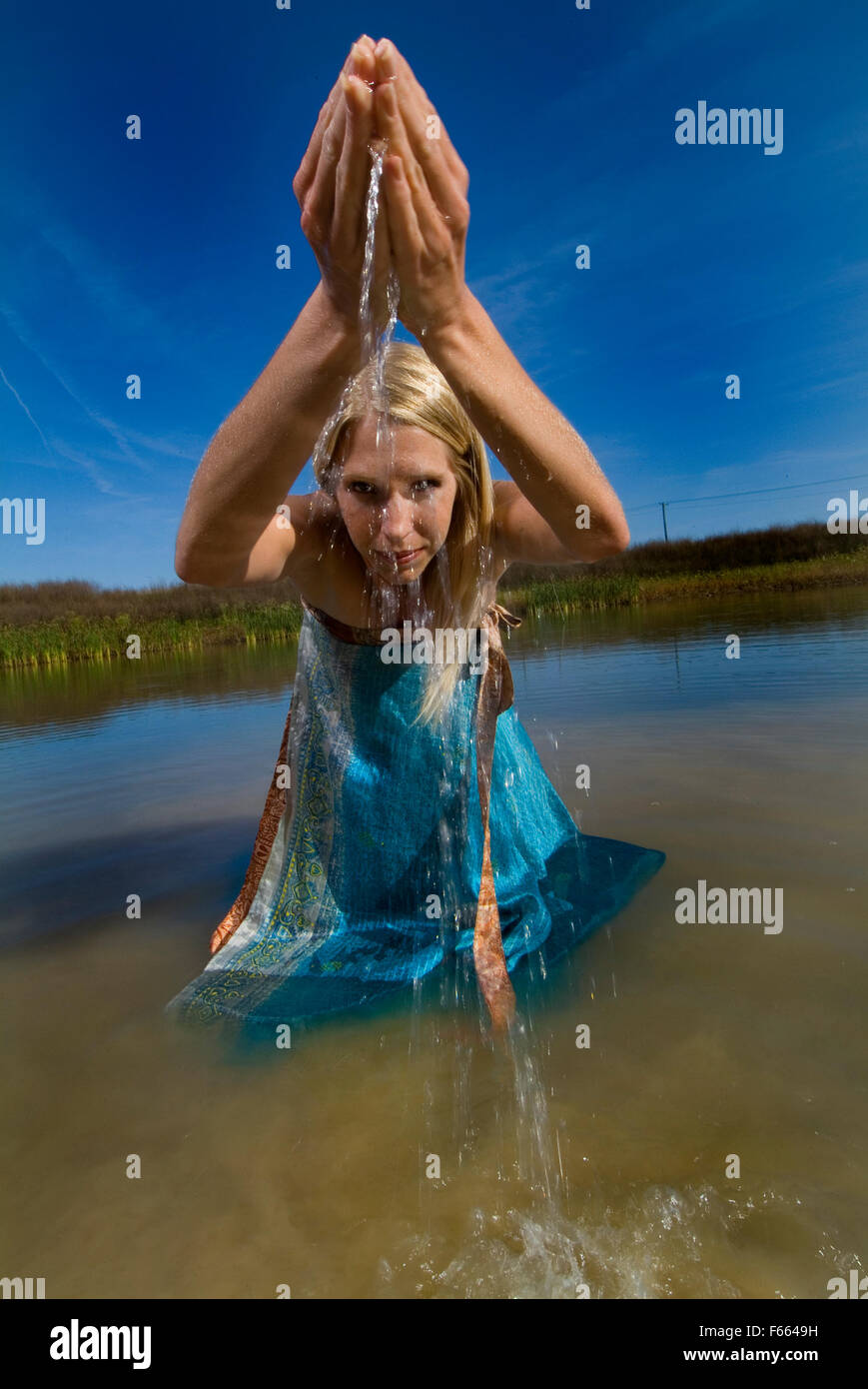 Eine blonde Frau in Wasser im freien Wasser nach oben und aus den Händen. Fülle Konzept, tolle blauer Himmel, riesige. Das Wasser ausgießen wird. Stockfoto