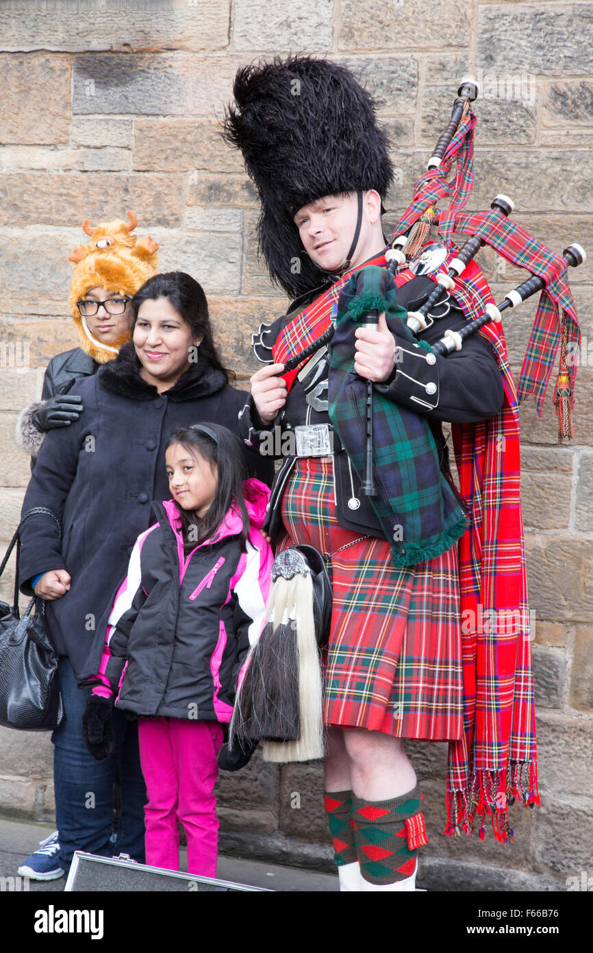 Eine Familie mit ihren Fotos, die mit einer traditionell gekleideten Scottish Piper, Edinburgh, Scotland, UK Stockfoto