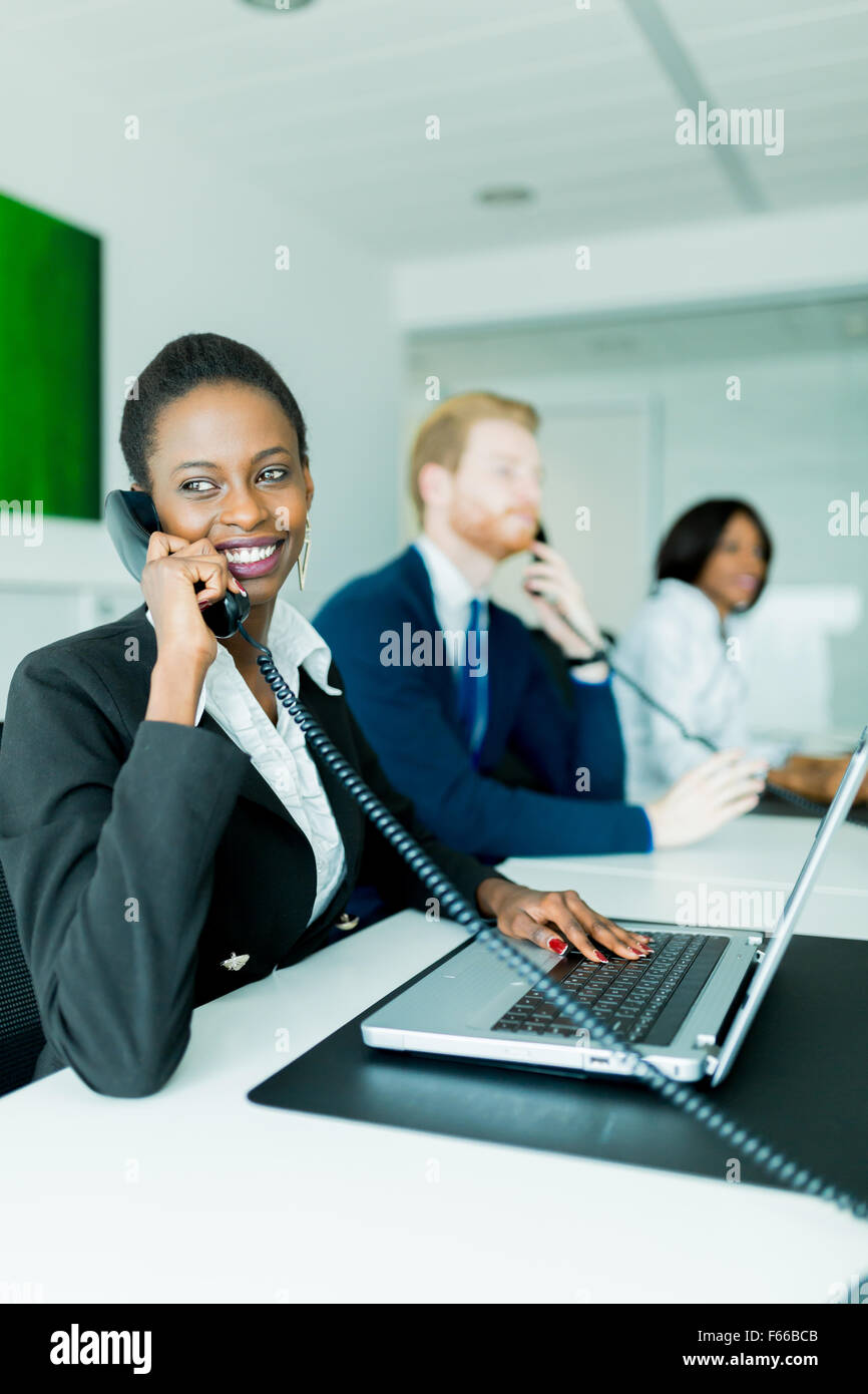 Eine schöne, schwarze, junge Frau arbeitet in einem Callcenter in einem Büro mit ihrem roten Haird Partner am anderen Ende des Schreibtisches ta Stockfoto