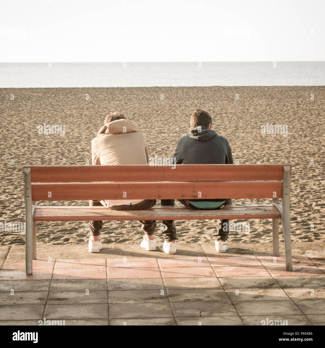 Zwei Jugendliche sitzen auf der Bank mit Blick auf Strand. Stockfoto