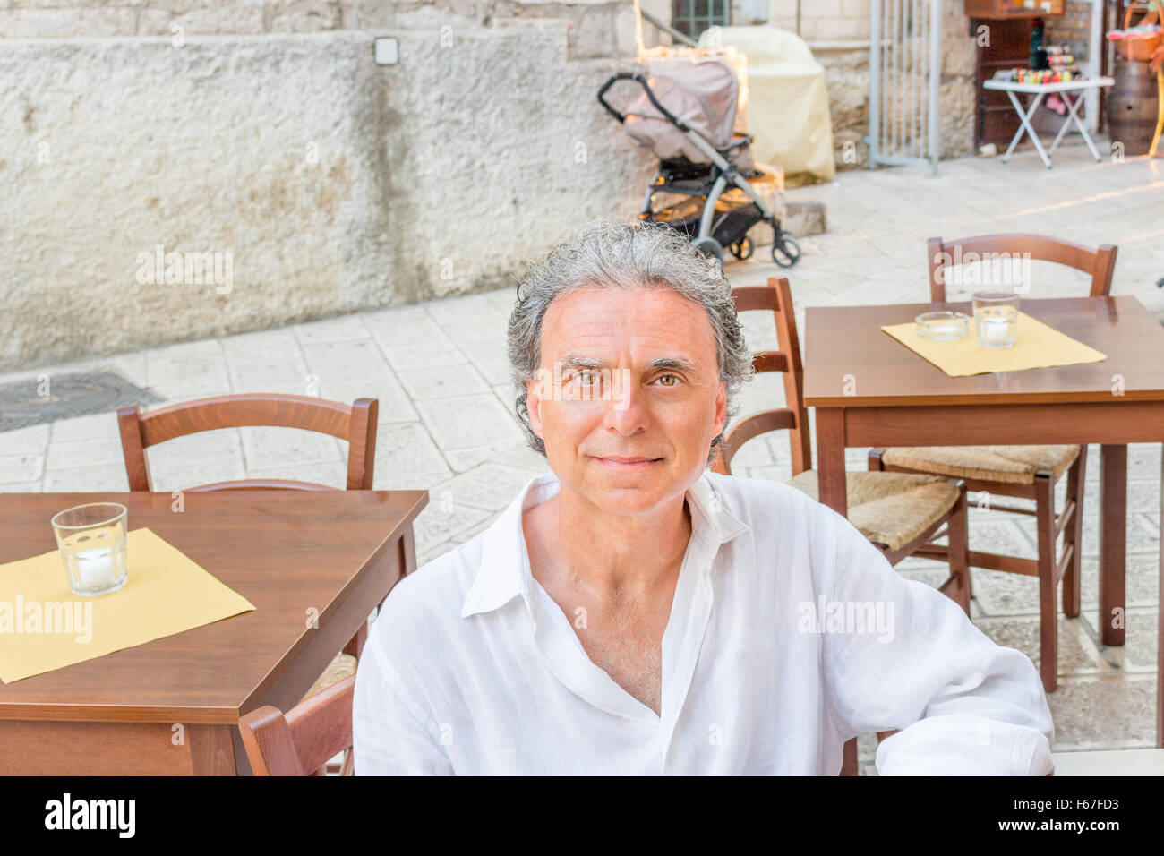 im mittleren Alter Mann im weißen Hemd sitzt im Restaurant bei einem Besuch in den alten Straßen der alten Stadt, in Italien, bekannt als die Perle des Gargano Vieste Stockfoto