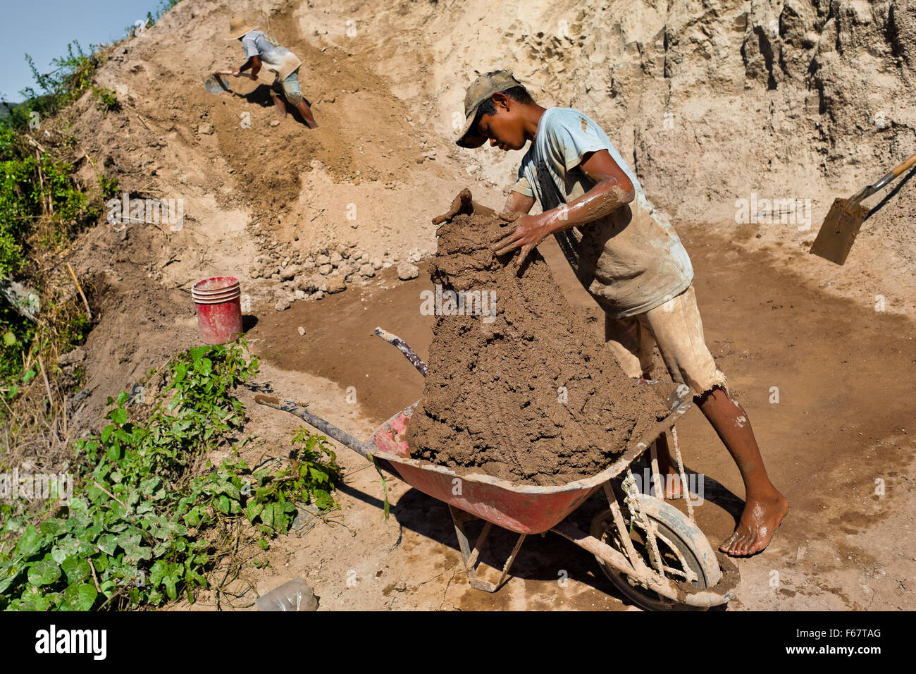 Moisés, ein El Salvador junge füllt Schubkarre mit Lehm für Ziegel Making an eine Ziegelei in Istahua, El Salvador. Stockfoto