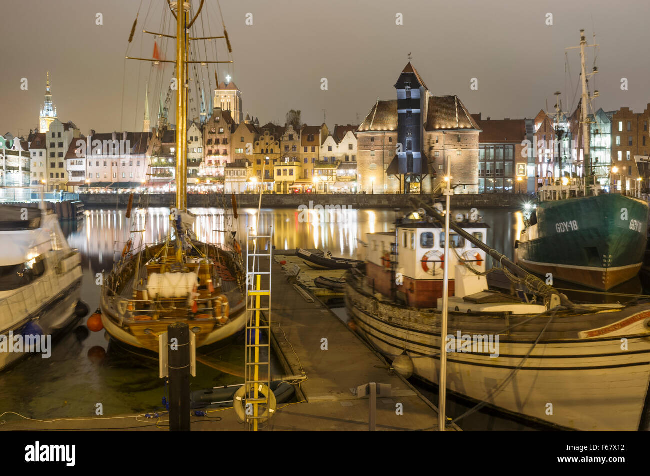Boote, mittelalterliche Kran und Waterfront Mietskasernen spiegelt sich auf der Mottlau durch Nacht verankert. Danzig, Polen Stockfoto