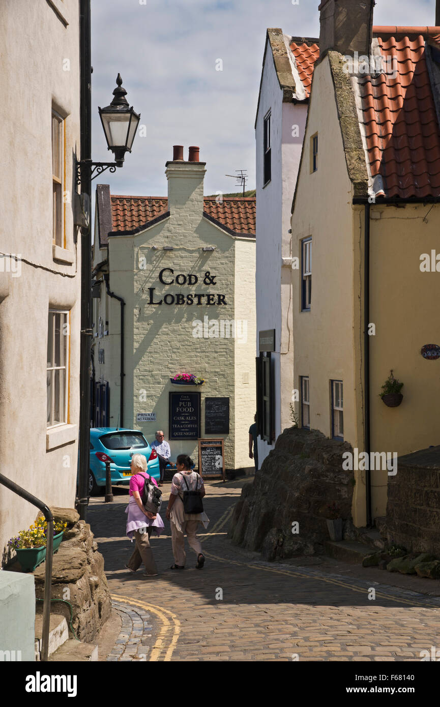 Besucher gehen Sie den malerischen, engen, gepflasterten Hauptstraße in dem traditionellen Fischerdorf Dorf Staithes, North Yorkshire, UK, an einem sonnigen Sommertag. Stockfoto