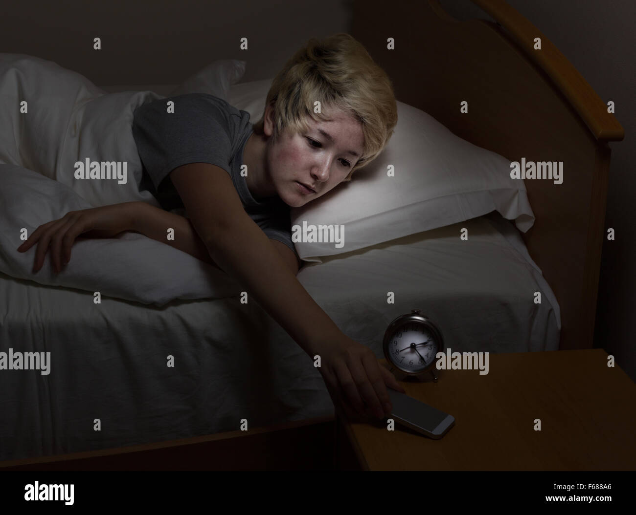 Teenager-Mädchen für ihr Handy, über Nacht stehen, während im Bett zu erreichen. Teen mit Technologie spät in der Nacht statt zu schlafen. Stockfoto