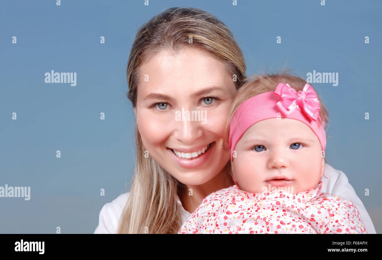 Closeup Portrait von fröhlich lächelnde Mutter mit schönen Mädchen auf Händen isoliert auf blauem Hintergrund, glückliches Familienleben Stockfoto