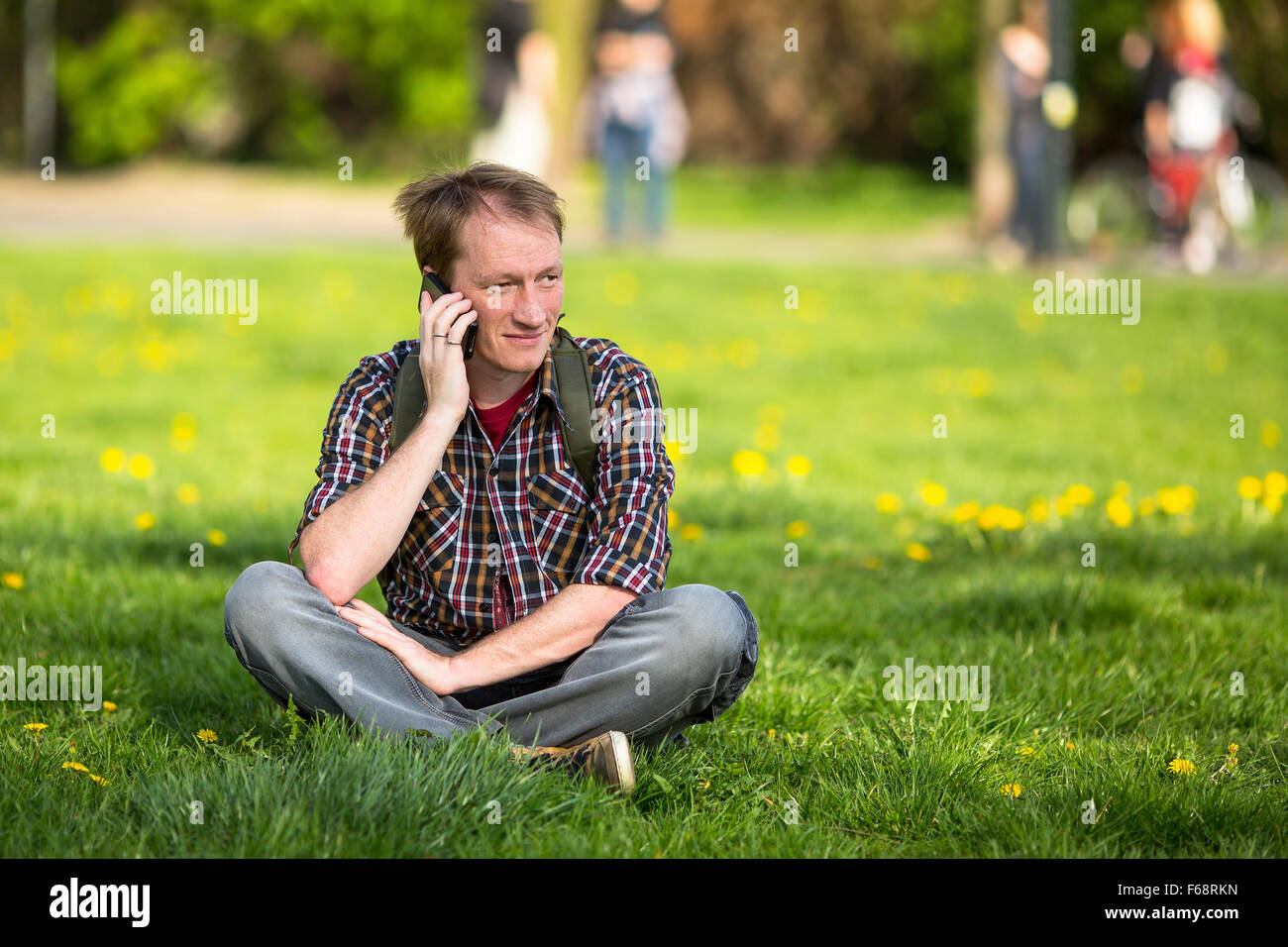 Junger Mann telefonieren mit Handy sitzen auf dem grünen Rasen im Park. Stockfoto