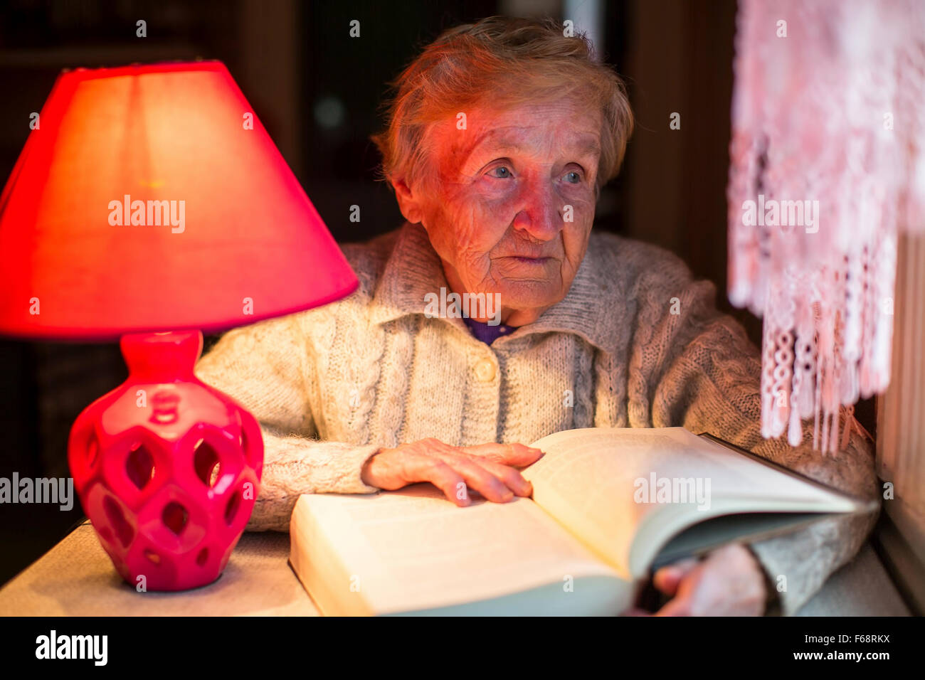 Ältere Frau liest ein Buch mit einer Tischlampe. Stockfoto