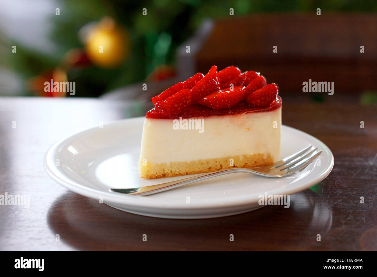 Frische Erdbeer Käsekuchen. Selektiven Fokus an der oberen Vorderkante des Kuchens. Weihnachtsbaum im Hintergrund Stockfoto